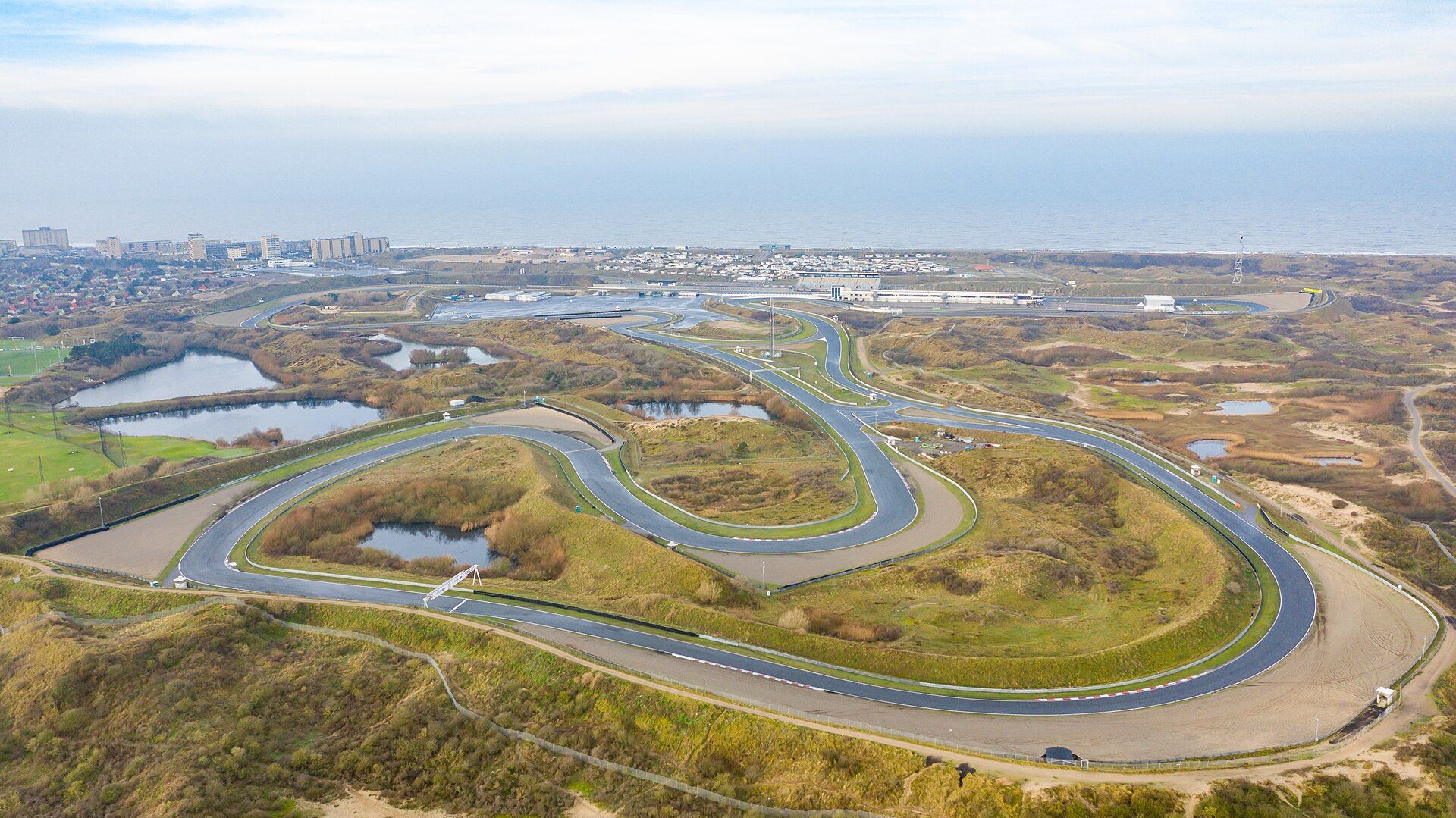 Zakręty toru Circuit Zandvoort wśród wydm i stawów, w tle zabudowa Zandvoort i Morze Północne