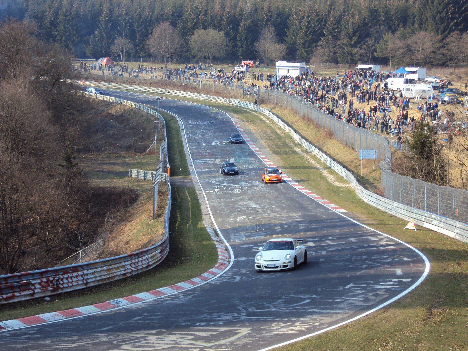 Sekcja Brünnchen pętli Nürburgring Nordschleife: samochody na asfalcie pokrytym napisami i widzowie na skarpie
